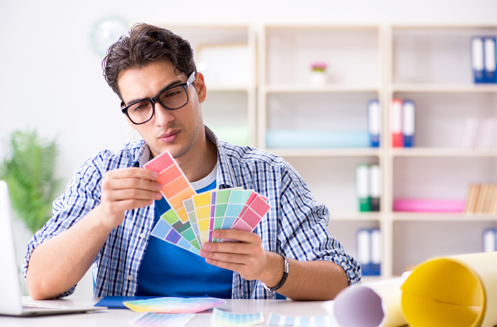 A focused man actively engaged in the design process, selecting colors for a room. Surrounded by color swatches and samples, he carefully considers various options. The image reflects a thoughtful and deliberate approach to creating a personalized and visually appealing room design.