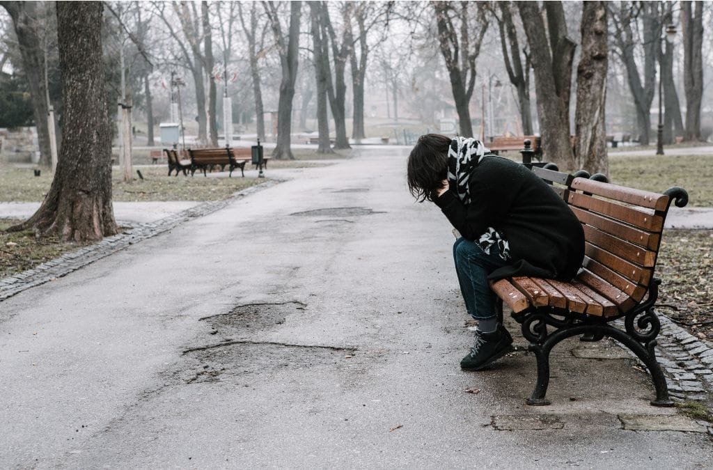 A person sitting alone on a bench, appearing sad, possibly due to seasonal affective disorder