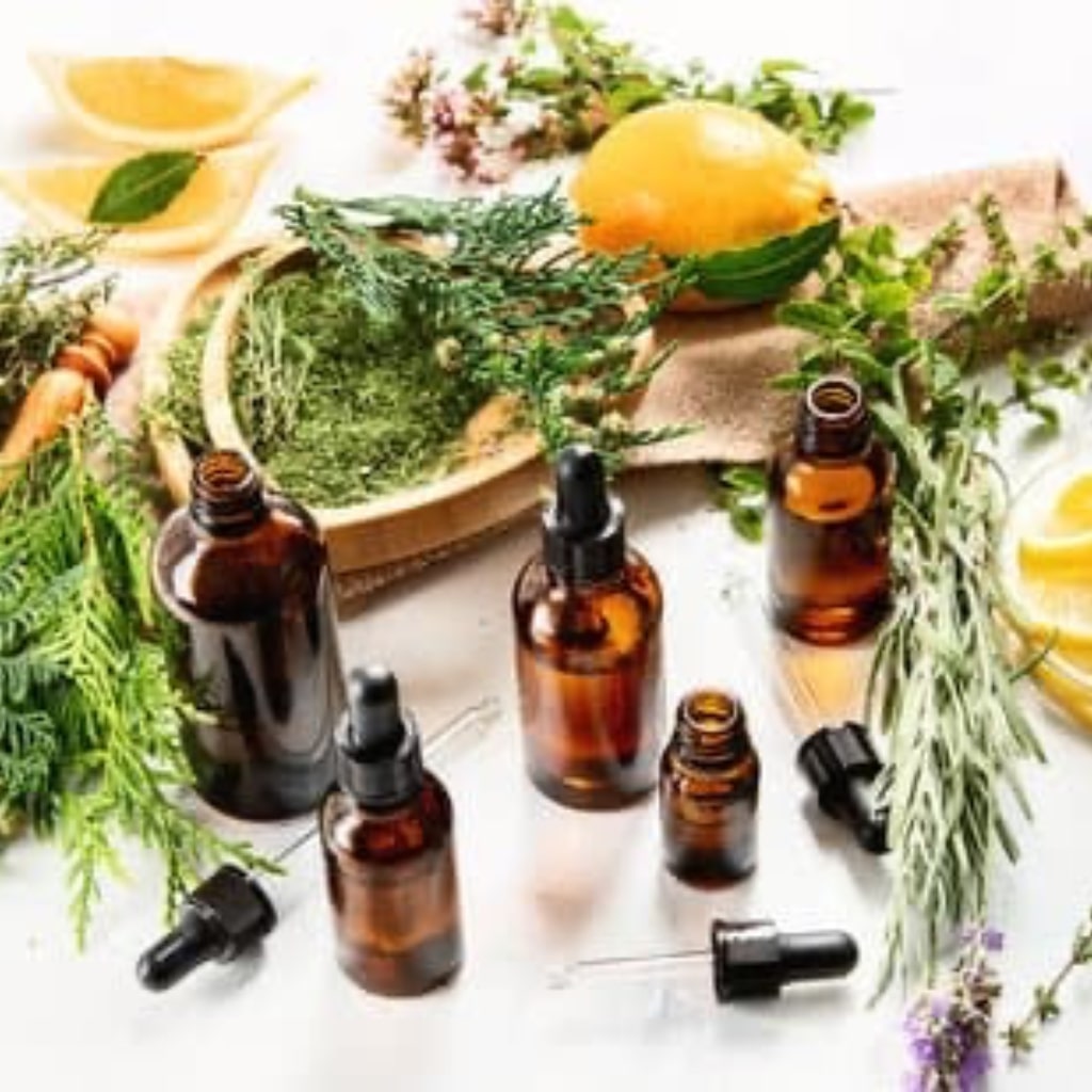 An assortment of essential oil bottles is arranged on a table, nestled amidst a backdrop of fresh herbs and vibrant lemons. The bottles exude an array of soothing colors, hinting at the diverse aromatic blends within. The scene captures the essence of natural wellness, with aromatic herbs and citrus adding a touch of freshness. The arrangement suggests a harmonious blend of fragrances, inviting a sensory journey through the world of essential oils and botanicals.