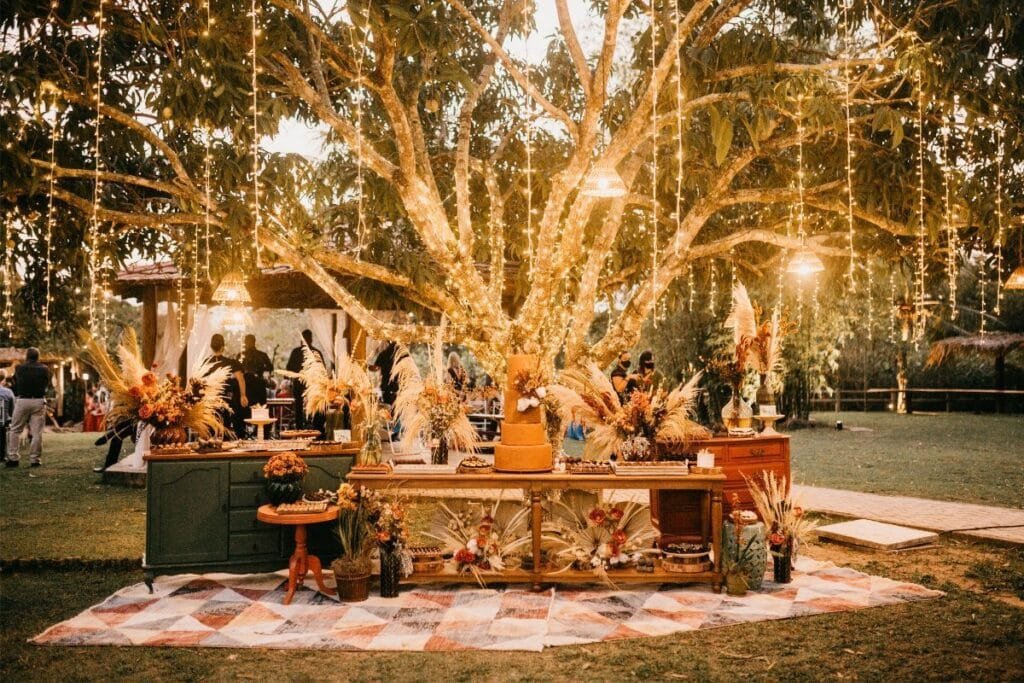 Vintage dessert table under a lit tree, decorated with pampas grass and dried flowers