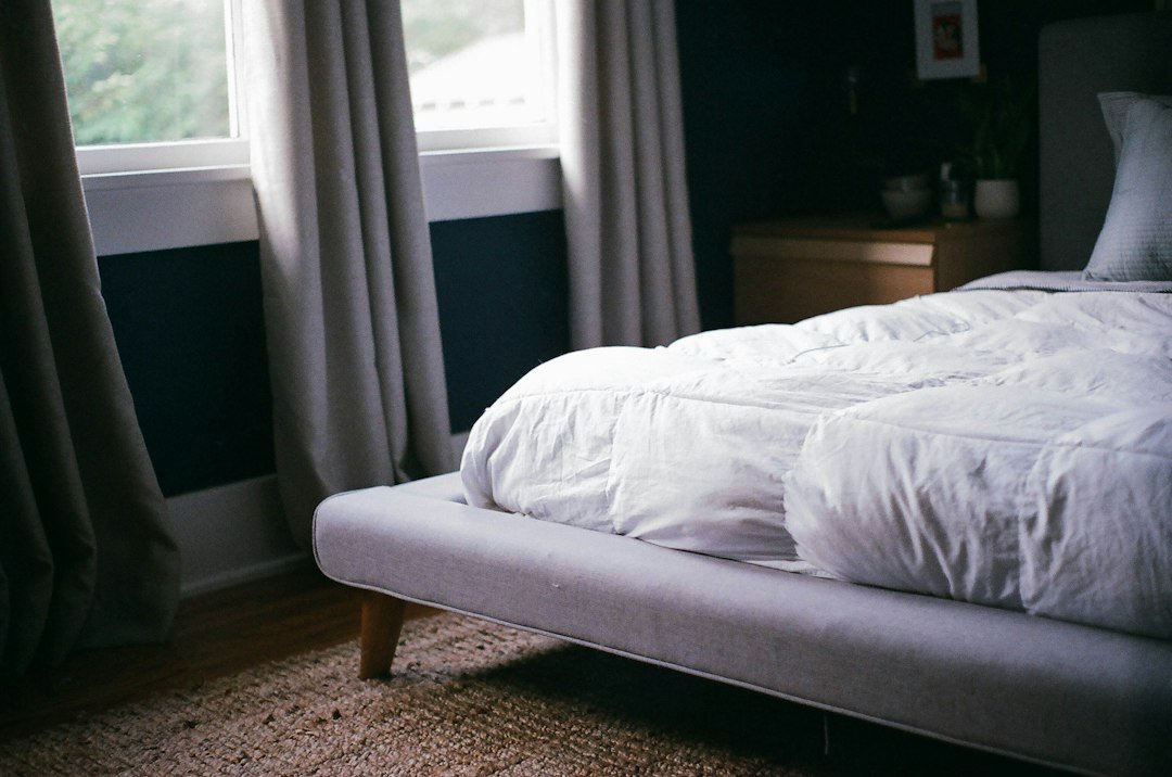 White duvet and comforter on a bed beside a window